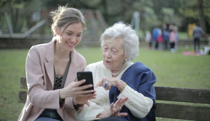 צעירה ואישה זקנה מסתכלים בטלפון על הספסל